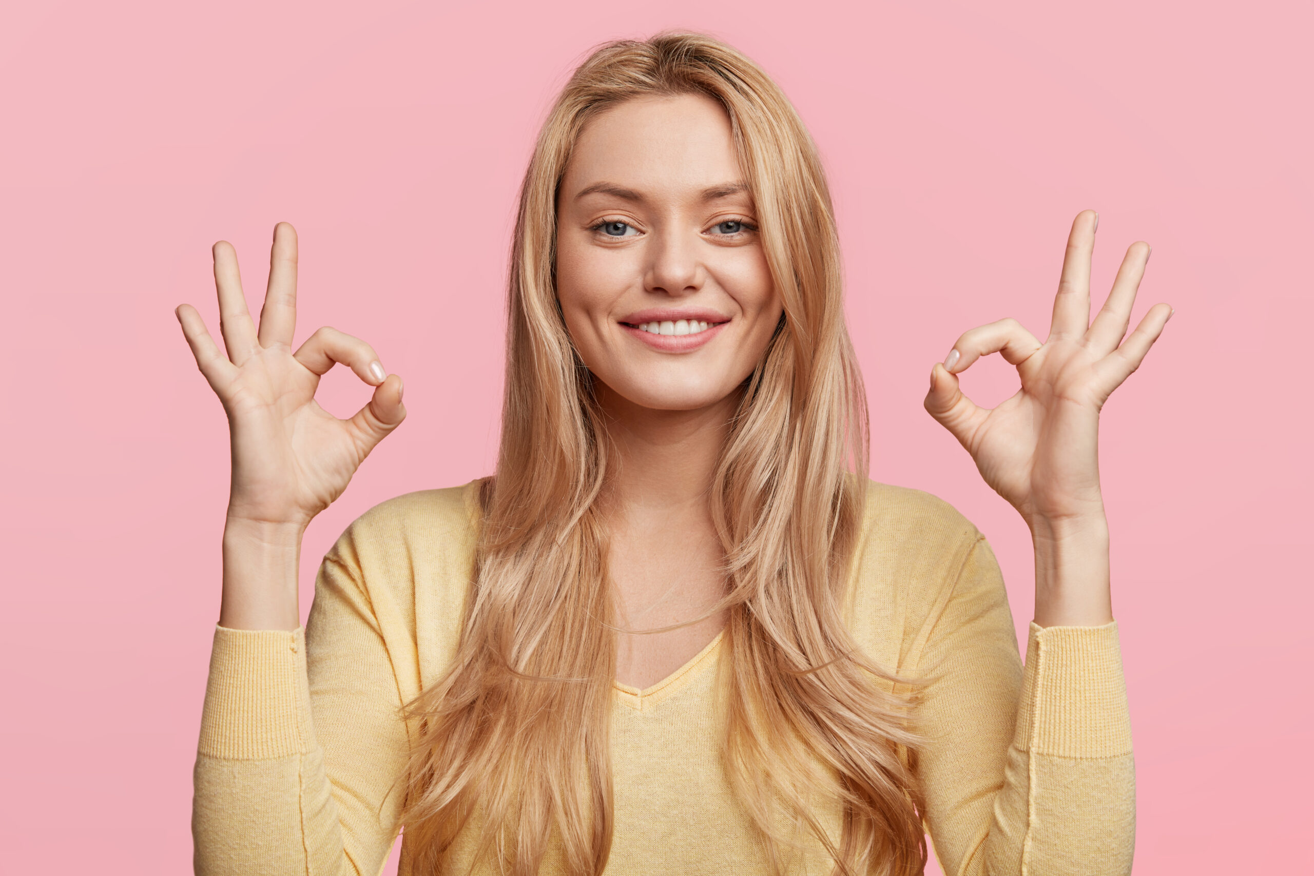 Smiling woman making an OK hand gesture, representing confidence and long-lasting results with proper dental implant care.